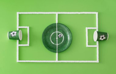 Futbol sahası ya da kağıt bardaklar, tabaklar ve açık yeşil arka planda şeker küpleriyle yapılmış futbol sahası. Minimum spor ya da yemek konsepti. Yaratıcı futbol partisi kompozisyonu. Düz yatıyordu, manzaranın tepesinde..