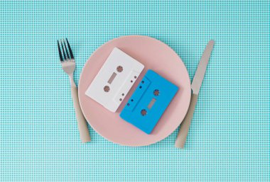 Beyaz ve mavi arka planda çatal ve bıçaklı pembe plakalı kasetler. Retro müzik fikri olan en az yemek. Retro teknolojinin yaratıcı konsepti. 80 'ler ya da 90' lar estetik vintage tarzı.