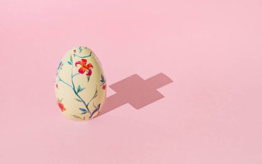Paskalya yumurtası ve pastel pembe arka planda Hıristiyan çapraz gölgesi. Asgari Paskalya konsepti. Yaratıcı bahar tatili planı. Işık ve gölge oyunlu orijinal bir arkaplan resmi.