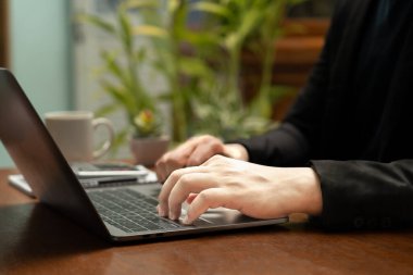 İş adamı masasında oturmuş, önemli rakamları ve hesaplamaları aynı anda yazmak için defterini kullanarak parlak dizüstü bilgisayarını kullanıyordu. Odaklanmış kararlılıkla. Not al..