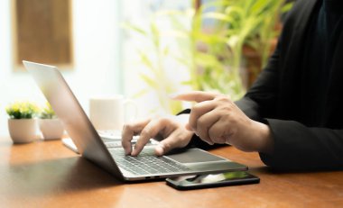 Meşgul işadamı işini becerikli bir şekilde dizüstü bilgisayarını, cep telefonunu ve hesap makinesini kullanarak yönetir, görevler ve hesap makineleri arasında sorunsuzca geçiş yapar,