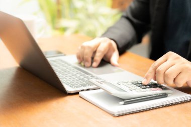 Meşgul işadamı işini becerikli bir şekilde dizüstü bilgisayarını, cep telefonunu ve hesap makinesini kullanarak yönetir, görevler ve hesap makineleri arasında sorunsuzca geçiş yapar,
