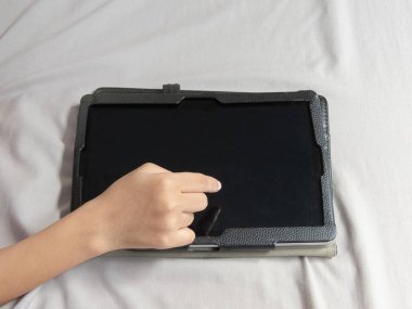 Küçük kız mutlu bir şekilde iPad 'iyle oynuyor, yatağında rahatça yatıyor. Yüzü sevinçle ışıldıyor ekranla etkileşime geçiyor. Önündeki büyüleyici dijital dünyaya kendini kaptırmış..