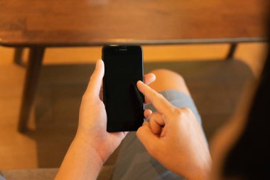 Gösterişli bir cep telefonunun erkek elinin sıkıca kavraması modern bir alışveriş deneyimini gözler önüne seriyor. Becerikli parmaklarıyla, çeşitli ürünleri keşfetmek için sanal bir pazar yerinde geziniyor. Yakından.