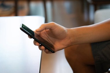 Gösterişli bir cep telefonunun erkek elinin sıkıca kavraması modern bir alışveriş deneyimini gözler önüne seriyor. Becerikli parmaklarıyla, çeşitli ürünleri keşfetmek için sanal bir pazar yerinde geziniyor. Yakından.