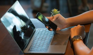 Kadın çevrimiçi alışveriş macerasına dalmış, cep telefonu ve dizüstü bilgisayarı arasında sorunsuzca geçiş yapıyor. Becerikli tıkırtılar ve tıkırtılarla geniş bir dijital pazarı keşfediyor..