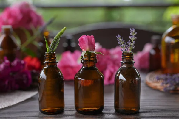 Glass bottles of different essential oils with plants against blurred background. Bottles of essential oil with fresh herbs and medicinal flowers. Side view.