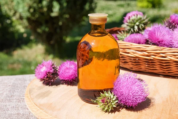 stock image Flower and burdock extract. Buds medicinal wild plants burdock and burdocks medicinal tincture from it. Bottles of herbal essential oil and flowers. Side view, copy space for text, product place.