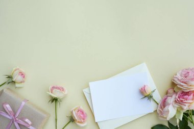 Açık pembe güller ve açık arkaplanda hediye arasında kağıt kart. Düğün maketi. Yatay boş kart ve pastel çiçeklerle romantik bir sahne. Sevgililer Günü, Bahar veya Anneler Günü. Düz yat, boşluğu kopyala.