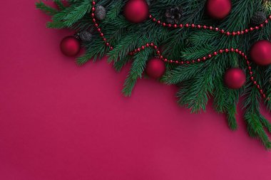 Kompozisyon, çerçeve köşesi koni ve toplarla birlikte Noel ağacı dallarından katlanmış. Kırmızı arkaplan ve metin için yer. Xmas ya da Yeni Yıl tebrik kartı şablonu. Üst görünüm, düz yatış. Kış tatili teması.