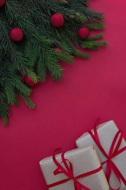 Noel kompozisyonu. Noel hediyesi, çam kozalakları, köknar dalları ve kırmızı arka planda Noel süslemeleri. Üst görünüm, düz görünüm, metin kopyalama alanı.
