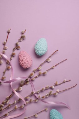 Pussy-willow twigs with Easter eggs on light purple background. Spring and Easter concept. Flat lay, top view. Space for text.