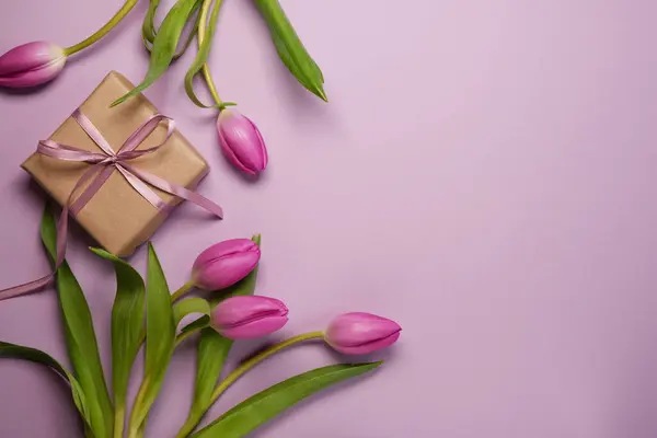 Mother\'s Day or International Womens-day concept. Top view of fresh tulips and kraft present on light purple background. Flat lay. Space for text.