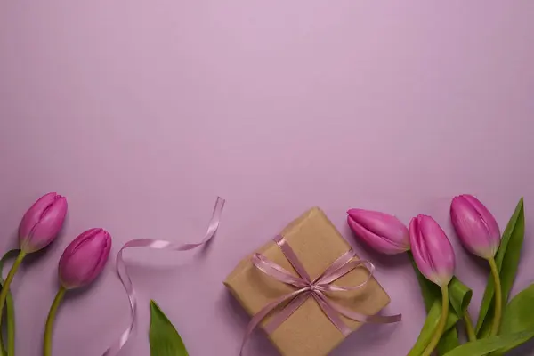 Mother\'s Day or International Womens-day concept. Top view flat lay of present boxes with ribbon, tulip flowers on a soft pastel violet background with space for text or advert.