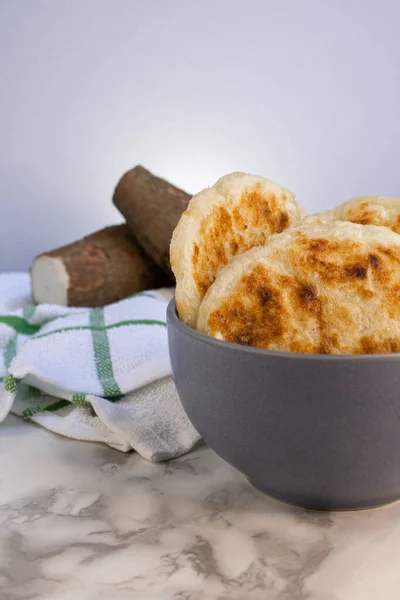 Arepas de yuca y queso tradicionales ecuatorianas junto a dos trozos de yuca cruda fresca