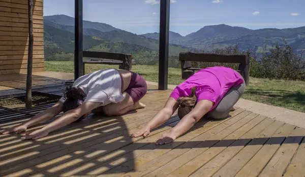 Two latin women doing yoga outdoors. Stretching exercise on a sunny day.