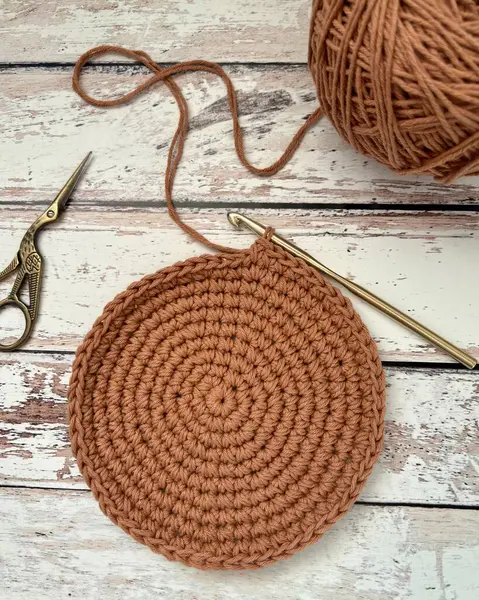 stock image Unfinished crochet round shape placemat on a wooden surface and a scissor on its side. High quality photo