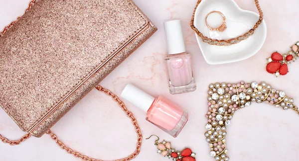 Rose gold flat lay fashion and jewelry concept with rose quartz background, pink nail polish, glitter clutch purse, and rose gold diamond jewelry