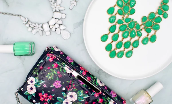 Green and white jewelry and nail polish flat lay with floral clutch purse outfit concept