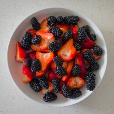 Bir kasede taze dilimlenmiş çilek ve böğürtlen
