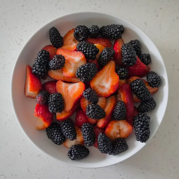 Bir kasede taze dilimlenmiş çilek ve böğürtlen