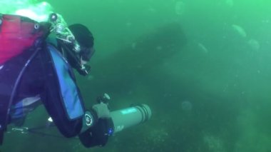 Diver with an underwater scooter moves in the water column through an accumulation of jellyfish.