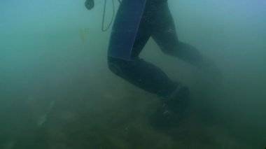 Profesyonel bir dalgıç nehir kıyılarının bulanık sularında deniz tabanında yürür, kamera dalgıcın ayaklarından kaskına doğru yükselir..