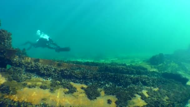 潜水员带着水下滑板车在生锈的残骸碎片上游动 然后从相机向太阳光飞去 — 图库视频影像