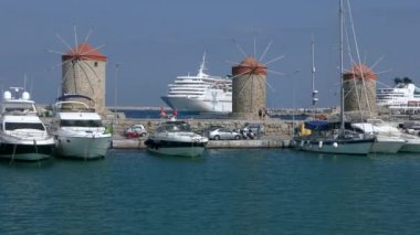 İskelede duran antik değirmenler ve yatlar, hareket halindeki bir geminin manzarası. Rodos, Yunanistan.