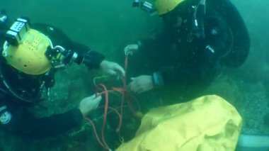 Underwater Archeology: Divers attach an underwater lifting bag to an antique Greek stone anchor.