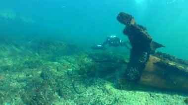 A diver with an underwater scooter swims against the concrete hydraulic structure between pieces of a wreck and leaves the frame.