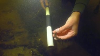 Underwater archaeological exploration: A diver demonstrates a metal brace on an 18th century wooden vessel lying on the bottom of a river, close-up.