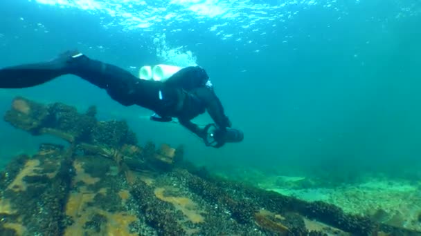 一名潜水员带着一辆水下滑板车在生锈的残骸上游泳 然后离开相机 — 图库视频影像