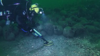 BLACK SEA, UKRAINE - 15 AĞUSTOS 2016: Sualtı Arkeolojisi: Metal dedektörlü bir dalgıç antik bir gemi enkazının yerini gösteren bir amfora kümesi yakınındaki deniz tabanını araştırıyor.