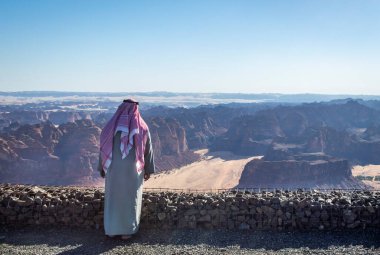 Alula, Suudi Arabistan, 4 Nisan 2024. Güneşli bir günde Harrat View Point 'ten Alula dağlarına bakan Suudi Arabistan' lı bir erkeğin arka görüntüsü. 
