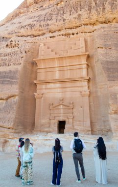 Alula, Suudi Arabistan, 4 Nisan 2024. Hegra 'daki taş mezarının önünde duran küçük bir turist grubunun arka görüntüsü.. 