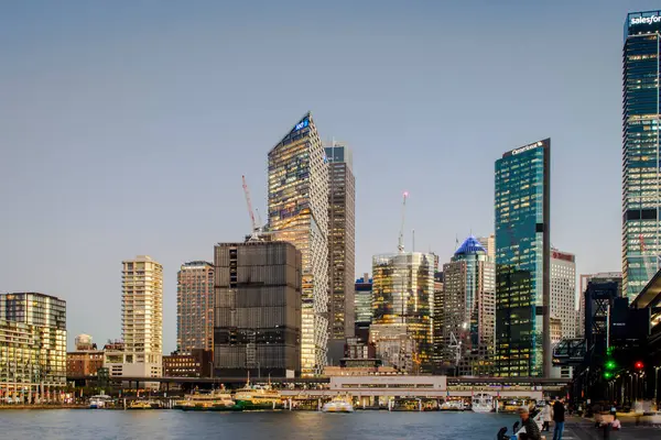 Sydney, Avustralya, 27 Temmuz 2023. Sydney şehir merkezinin ufuk çizgisi, akşam vakti renkli ışıklarla aydınlatılan dairesel rıhtımın su manzarası..