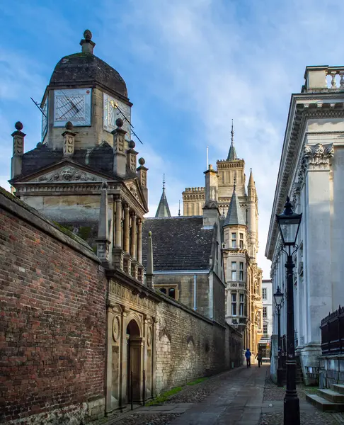 Cambridge, İngiltere, 7 Ocak 2022. Güneşli bir günde Cambridge 'de tuğla duvar ve eski saat kulesiyle dar bir cadde manzarası. 
