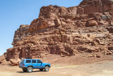 Alula, Suudi Arabistan, 3 Nisan 2024. Güneşli bir günde Alula Dadan mirası sahasında arka planda mezarları ve kaya dağları olan mavi bir araba görülüyor..  