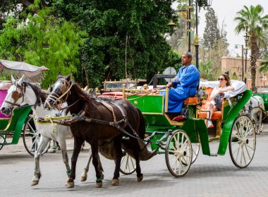 Marakeş, Fas, 8 Nisan 2023. Faslı bir erkek, güneşli bir günde Koutoubia Camii 'nin arkasında bir kadın turistle at arabasına biniyor.. 