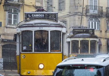 Lizbon, Portekiz, Mart 07, 2025. İkonik sarı Tramvay 28 yağmurlu bir günde Lizbon şehir merkezinin tarihi caddelerinde ilerliyor.  