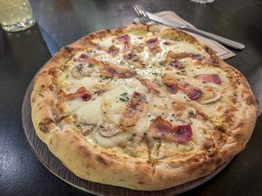 Restoranın yemek masasına erimiş peynirli ve jambonlu taze İtalyan pizzası. 