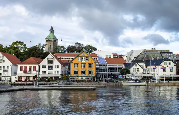 Norveç 'teki Stavanger limanının rıhtım manzarası. Renkli ahşap evler, tekneler ve sakin su günbatımında dramatik bulutlar altında..