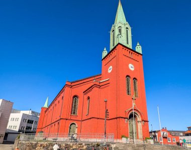 Stavanger, Norveç, 6 Haziran 2025. Stavanger St. Petri Kilisesi 'nin güneşli bir günde canlı bir kırmızı tuğla cephe ve açık mavi gökyüzüne kurulmuş yeşil bir kule manzarası..