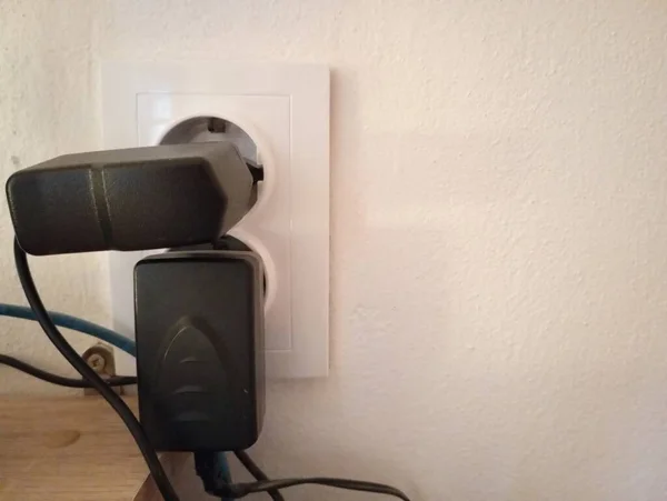 Two black power adapters are plugged into the white double socket on the wall at the same time.