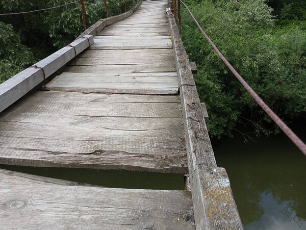 An extreme river crossing made of old rotten boards. Suspension bridge for pedestrians.