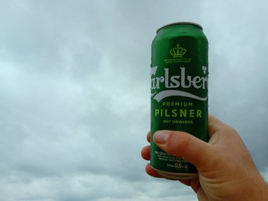 Kornalovichi köyü, Sambir bölgesi, Lviv bölgesi, Ukrayna - 14 Eylül 2023: Bir adam elinde bulutlu bir gökyüzünün arka planına karşı yeşil bir Carlsberg birası tutuyor.