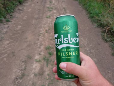 Kornalovichi köyü, Sambir ilçesi, Lviv bölgesi, Ukrayna - 14 Eylül 2023: Bir adamın elinde bir kır yolunun arka planında yeşil bir Carlsberg birası var.