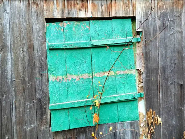 Yıkılmış ahşap bir evin eski eğri bir penceresi yeşil ahşap panjurlarla kaplıdır..
