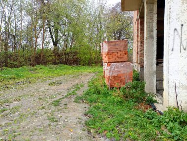 Yarım kalmış bir binanın yakınındaki özel paletlerde tuğlalar var. Bitmemiş inşaat ve endüstri konusu.